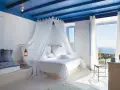 Camera da letto stile mediterraneo con soffitto blu, letto a baldacchino bianco e vista mare.
