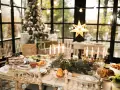Un tavolo imbandito per Natale, con torta, arrosti e candele. Un modo perfetto per come addobbare la cucina per Natale, con un albero illuminato sullo sfondo.