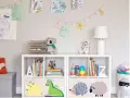 Soluzione creativa per come sistemare i giochi in salotto: scaffali bianchi con contenitori decorati e libri ordinati.