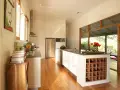 Cucina moderna con isola centrale dotata di una cantina a vista per il vino. Ampie vetrate si aprono su un patio esterno.