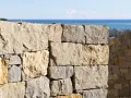 Muro a secco per contenimento terra, con vista sul mare e un borgo in lontananza.
