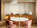 Una casa colorata con un'isola cucina arancione, sedie rosa e un tavolo bianco. Un vaso di fiori aggiunge un tocco di vivacità.