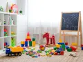 Un angolo pieno di giochi colorati, blocchi, un camioncino, un cavallo a dondolo e una lavagna: perfette idee stanza giochi bambini per stimolare la creatività.