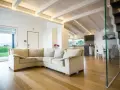 Soggiorno moderno con travi in legno sbiancate senza carteggiare, divano beige e cucina a vista.