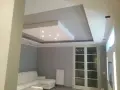 Soffitto moderno con velette in cartongesso, faretti incassati e illuminazione indiretta. Divano bianco e porta finestra.