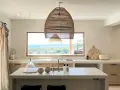 Cucina luminosa con isola centrale, lampadario in rattan e vista mare. Arredamento in stile casa bohemien con materiali naturali.