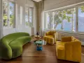 Un salotto con divano verde curvo e poltrone gialle, tavolini rotondi e vista lago. Un perfetto esempio di **art deco arredamento** con tocchi moderni.