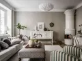 Salotto accogliente con camino in maiolica, divano grigio e pouf decorato. L'arredamento stile classico si fonde con elementi moderni.