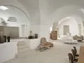 Interni moderni con soffitti a volta, un'elegante cucina a vista, zona living con divani e poltrone in vimini, e dettagli decorativi in ceramica.
