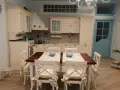 Accogliente piccola tavernetta casa con cucina in legno chiaro, tavolo da pranzo e porta azzurra.