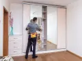 Un uomo con una borsa degli attrezzi controlla un armadio ante scorrevoli, forse per risolvere problemi di scorrimento o montaggio.