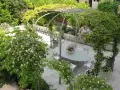 Un angolo incantevole per idee giardino villa: un pergolato metallico abbraccia un tavolo ovale con sedie, circondato da fioriture rosa e verdi rigogliosi.