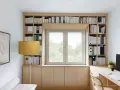 Una libreria a ponte in legno chiaro incornicia una finestra, con libri ordinati e un'area studio funzionale.