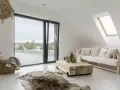 Salotto con divano bianco, tavolino grezzo e tappeto in pelle. Lampadario in perline e cesto in vimini completano l'arredamento boho chic.