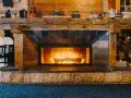 Camino in pietra e legno, con fuoco acceso, che evoca idee camini rustici di montagna. Sopra, oggetti d'epoca e legna accatastata.