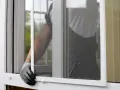 Mano con guanto che monta una zanzariera fai da te su una finestra.