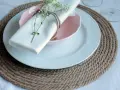 Sottopiatti in stoffa fai da te, con tovagliolo bianco legato da spago e decorato con un rametto fiorito.