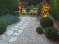 Giardino pavimentato con aiuole di lavanda e cespugli. Due sedie verdi con cuscini rosa invitano al relax.