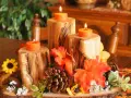 Un semplice centrotavola autunnale con tronchi di legno, candele arancioni, pigne e foglie colorate.