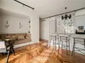 Open space con ingresso aperto su soggiorno. Divano angolare, bancone cucina con sgabelli e parquet a spina di pesce.