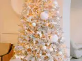 Albero di Natale innevato con luci calde, palline bianche e dorate, e decorazioni a forma di angeli e cervi. Un'elegante idea per un albero di Natale bianco e oro.