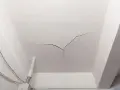 Crepe sul soffitto, un segno che il tempo o un problema strutturale sta lasciando il suo segno. Cavi elettrici e un tubo corrono lungo il muro.