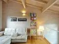 Soggiorno accogliente con divano bianco, libreria a giorno e un suggestivo tetto in legno a vista.