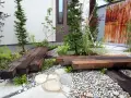 Un piccolo giardino zen con panchine in legno riciclato, ghiaia e piante verdi. Perfetto per idee giardino piccolo fai da te.