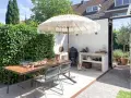 Accogliente zona barbecue esterna con tavolo in legno, sedie, ombrellone e un cane Shiba Inu che si rilassa.