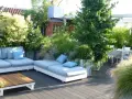 Un lussureggiante giardino sul terrazzo fai da te con divani comodi, tavolino in legno e un tavolo da pranzo.