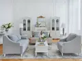 Salotto luminoso in stile shabby chic contemporaneo, con divani grigi, mobili bianchi e dettagli dorati.