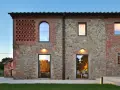Esterno di case stile toscano con muri in pietra e mattoni, finestre ad arco e rettangolari, illuminazione calda.