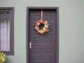 Ghirlanda natalizia appesa con un nastro alla porta scura, un esempio di come appendere la ghirlanda alla porta per le feste.