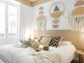 Accogliente camera da letto stile boho con decorazioni murali geometriche, tessuti naturali e un letto invitante.