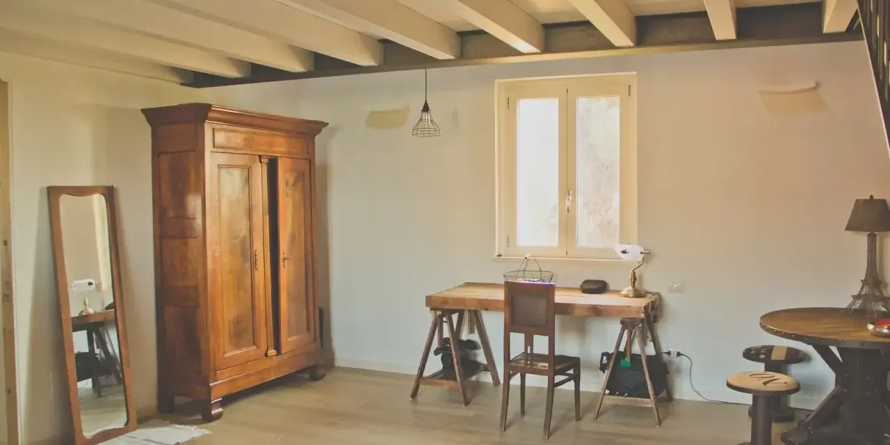 Arredamento casa di campagna: armadio antico in legno, specchio, scrivania rustica con sedia, tavolino rotondo e lampada a forma di Torre Eiffel.