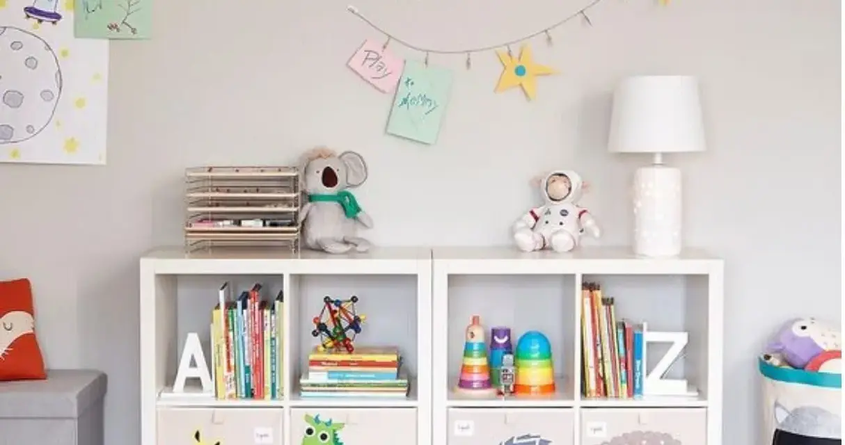 Soluzione creativa per come sistemare i giochi in salotto: scaffali bianchi con contenitori decorati e libri ordinati.