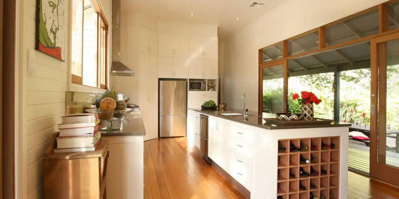 Cucina moderna con isola centrale dotata di una cantina a vista per il vino. Ampie vetrate si aprono su un patio esterno.