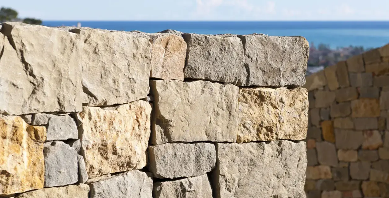 Muro a secco per contenimento terra, con vista sul mare e un borgo in lontananza.