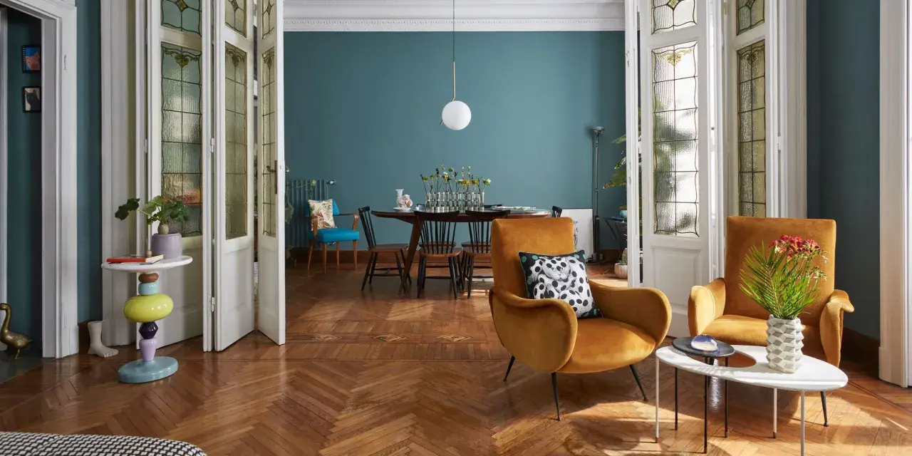 Salotto con poltrone ocra, tavolino dal design moderno e porte a soffietto con vetri decorati, un mix di stile vintage e contemporaneo.