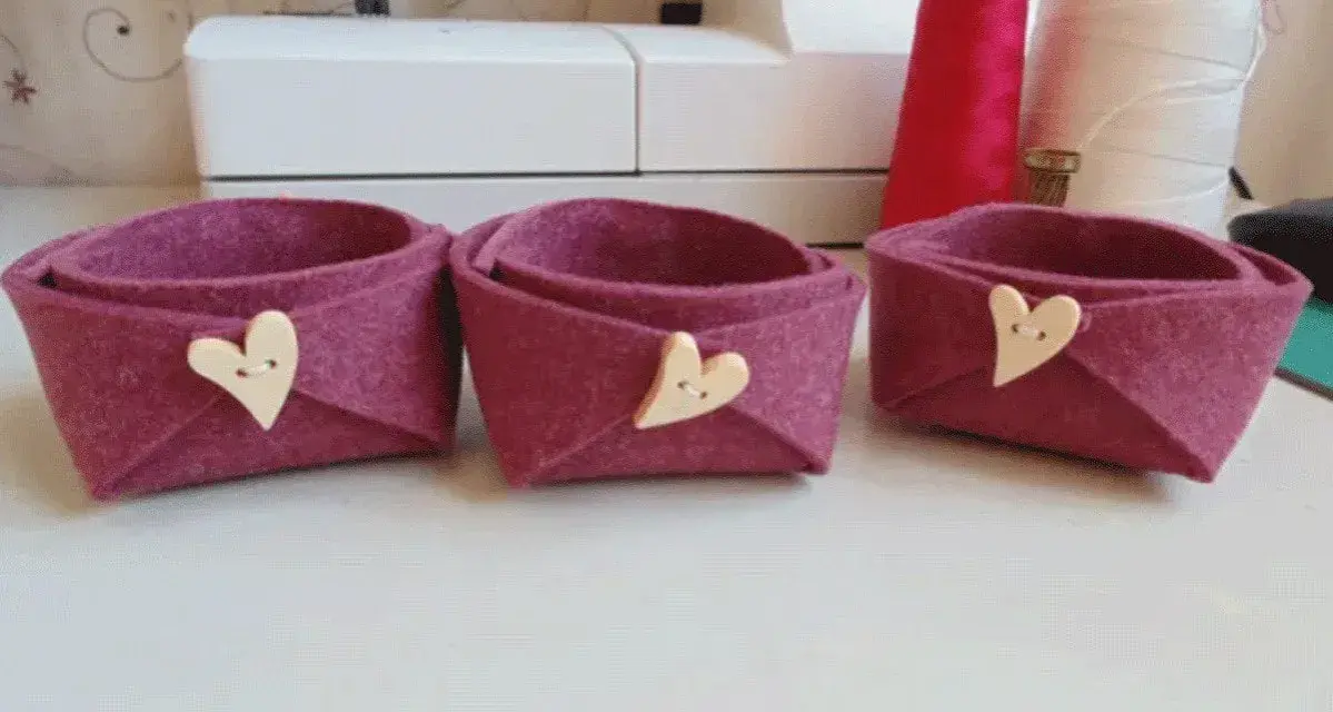 Tre cestini in feltro fai da te, color melanzana, decorati con bottoni a forma di cuore. Perfetti per organizzare piccoli oggetti.