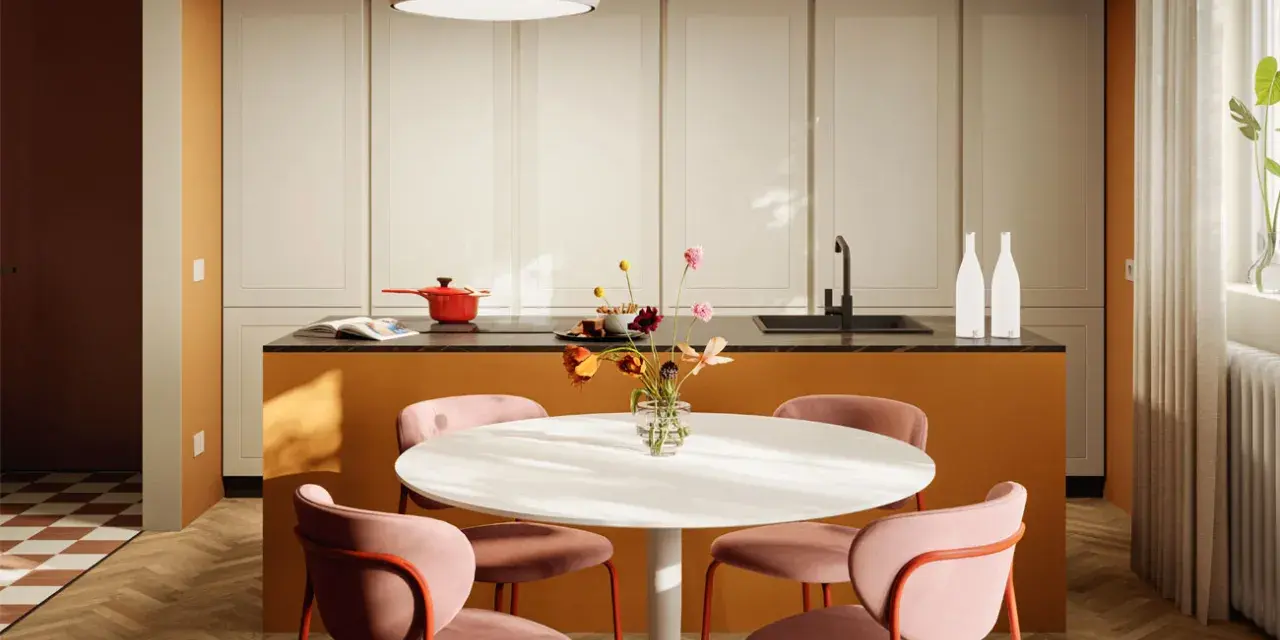 Una casa colorata con un'isola cucina arancione, sedie rosa e un tavolo bianco. Un vaso di fiori aggiunge un tocco di vivacità.