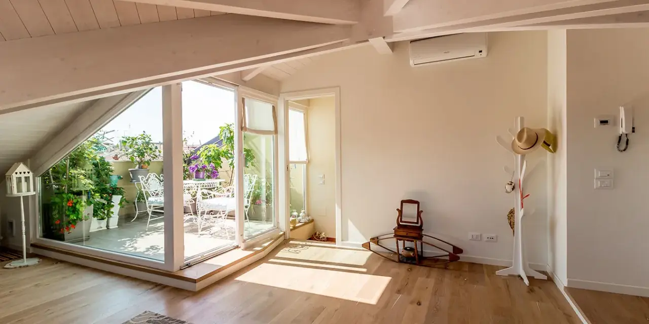 Luminoso sottotetto con travi a vista e un terrazzo fiorito. Idee sottotetto molto basso per sfruttare ogni angolo.