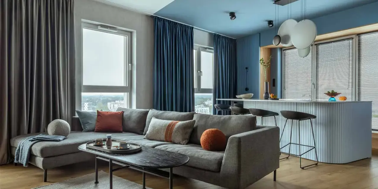 Soggiorno moderno con divano grigio, tavolino nero e tende blu e grigie. Un esempio di come scegliere le tende per il salotto per un look sofisticato.