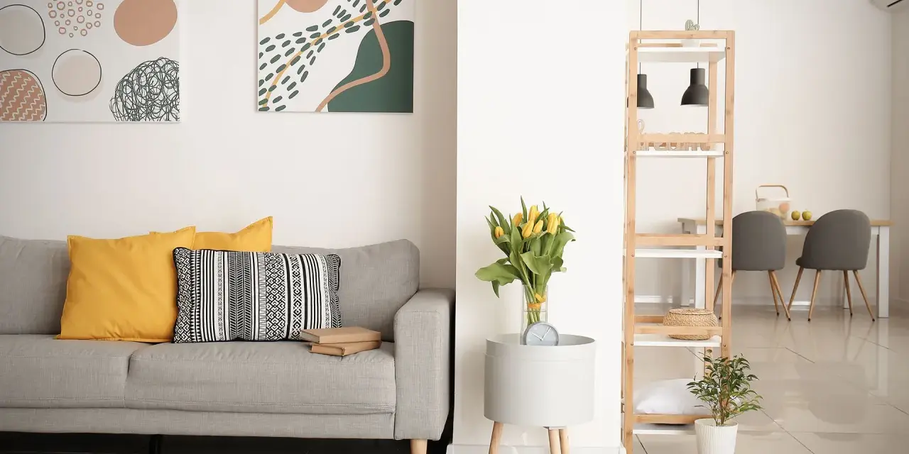 Soggiorno moderno con divano grigio, cuscini gialli e decorazioni astratte. Si nota la differenza tra ammobiliato e arredato: qui, ogni elemento è scelto con cura per creare un ambiente accogliente.