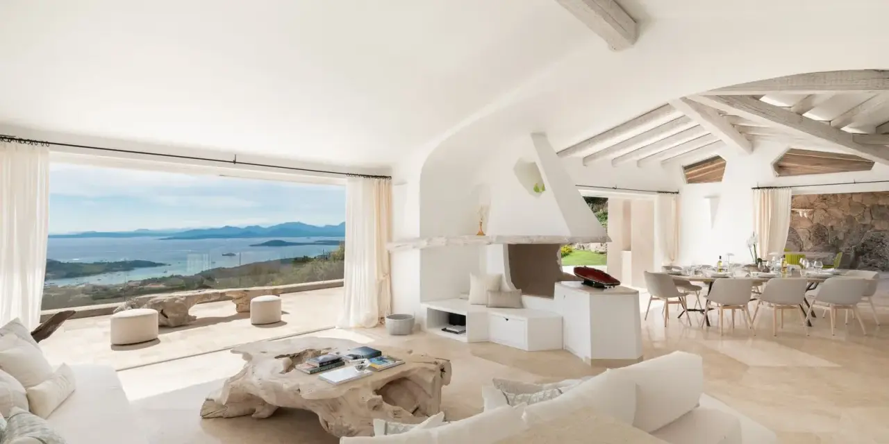 Soggiorno luminoso con vista mare, perfetto per l'arredo case al mare. Divani bianchi, camino moderno e tavolo da pranzo per godersi il panorama.
