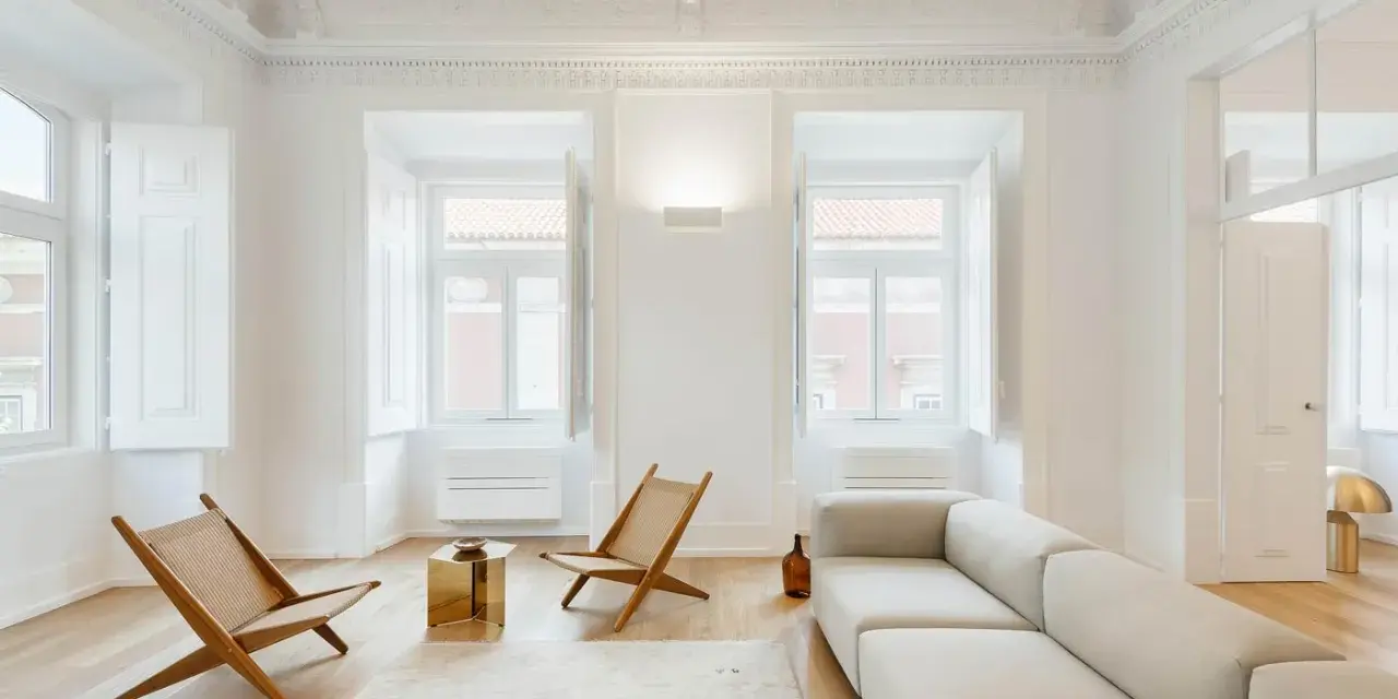 Soggiorno minimalista con divano chiaro, sedie in legno e tavolino dorato. Un esempio di come un consulente d'arredo può creare un ambiente luminoso e accogliente.