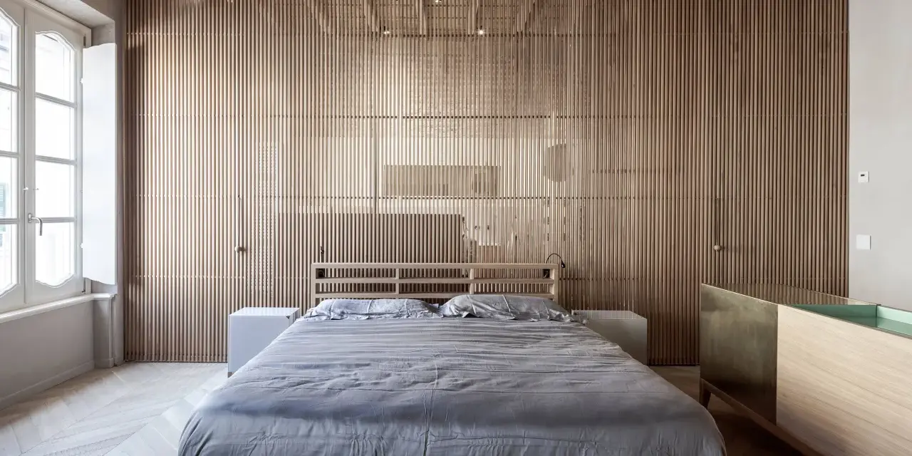 Camerette con separè in legno che creano un ambiente caldo e moderno. Letto matrimoniale con biancheria grigia e comodini bianchi.