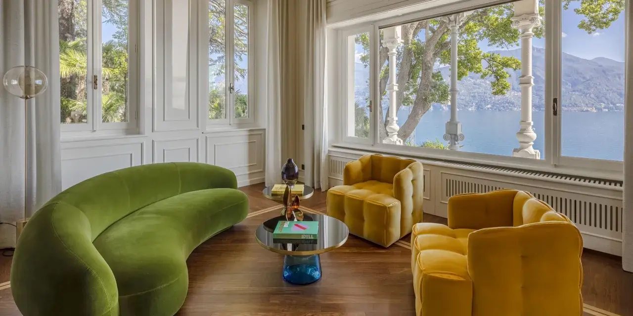 Un salotto con divano verde curvo e poltrone gialle, tavolini rotondi e vista lago. Un perfetto esempio di **art deco arredamento** con tocchi moderni.