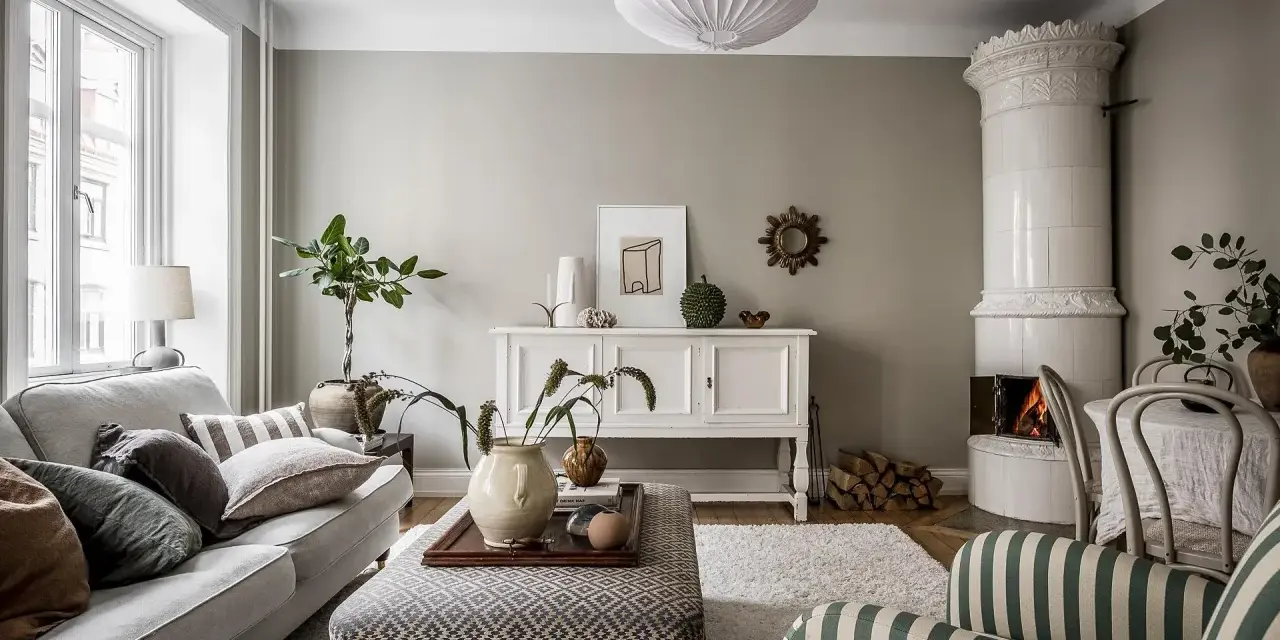 Salotto accogliente con camino in maiolica, divano grigio e pouf decorato. L'arredamento stile classico si fonde con elementi moderni.
