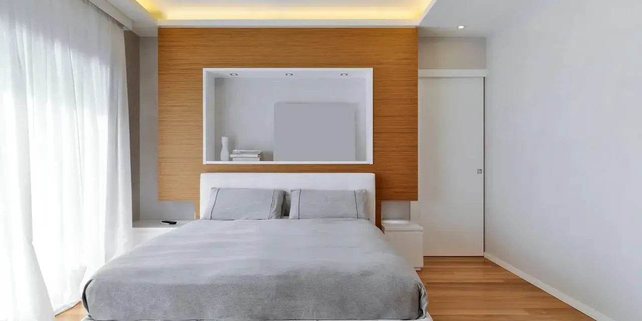 Camera da letto con letto bianco, lenzuola grigie e un moderno controsoffitto con illuminazione a LED.